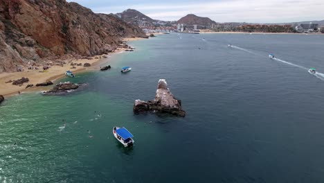 Pelican-rock,-touristic-attraction-at-Cabo-San-Lucas,-tour-boats-on-blue-sea,-Aerial-orbit-view
