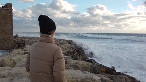 A-girl-looking-out-to-sea-as-the-waves-crash-against-the-rocks