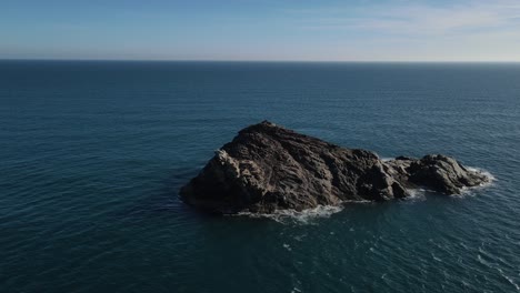 A-drone-flyover-of-a-lone-natural-rock-island-in-the-middle-of-the-clear-blue-waters-of-the-Mediterranean-Sea