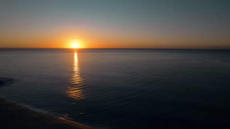 Drone-Flyover-Beautiful-sunrise-over-the-Pacific-Ocean,-Sunlight-reflections-on-water-surface