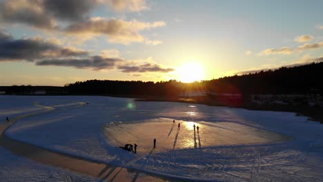 Luftaufnahme-Von-Menschen,-Die-Im-Winter-Bei-Sonnenuntergang-Auf-Einem-Zugefrorenen-See-Hockey-Im-Freien-Spielen