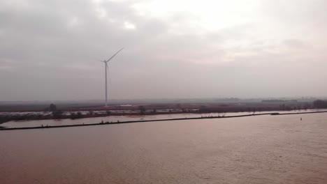 Aerial-View-Over-Oude-Maas-With-Single-Wind-Turbine-Seen-On-Overcast-Day-In-Distance-In-Barendrecht