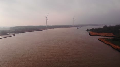 Aerial-Flying-Over-Oude-Maas-With-Wind-Turbines-Seen-Through-Misty-Clouds-In-Distance-In-Barendrecht
