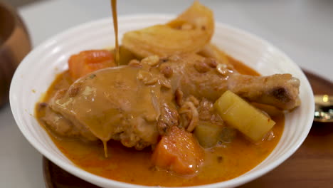 Preparar-Curry-Massaman-Con-Muslo-De-Pollo,-Verter-Rica-Y-Sabrosa-Salsa-De-Curry-Thai-Mussaman-Sobre-Pollo-En-Tazón-Blanco