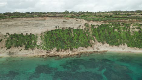 AERIAL:-Il-Hofra-l-Kbira-Bay-Limestone-Steep-Slope-on-Cloudy-Day-with-Mediterranean-Sea-Washing-Shores