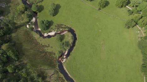 Drohnenaufnahme-Eines-Flusses,-Der-Durch-Eine-Grüne-Wiese-Fließt