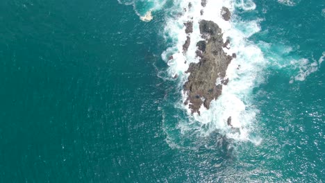 Rocks-being-hit-by-strong-ocean-waves-near-coastline-of-Indonesia,-aerial-top-down-orbit-view