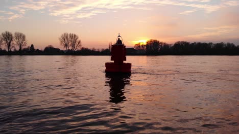 Low-Aerial-Flying-Past-Floating-Buoy-In-River-Against-Sunet-Skies