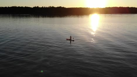 Aerial-view-of-a-man-using-his-paddleboard-in-a-lake-during-sunset
