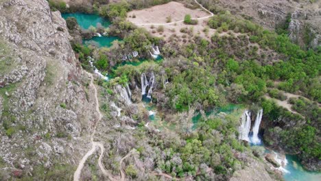 A-cinematic-panning-aerial-shot-over-beautiful-sloping-gem-toned-rivers-and-waterfalls,-and-the-lush-terraced-land-around-them-in-the-Krka-National-Park-in-southern-Croatia