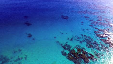 Topdown-ascending-vibrant-blue-sea-with-submerged-rocks,-Pacific-ocean
