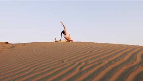 Young-brunette-yoga-instructor-on-a-sand-hill-performing-a-morning-yoga-routine-during-golden-hour