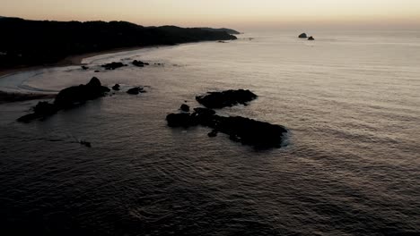Aerial-tilt-up-shot-of-peaceful-coastline-of-Punta-Cometa-Coastline-with-rocks-in-Oaxaca,Mexico---Beautiful-evening-with-yellow-sunset-in-backdrop