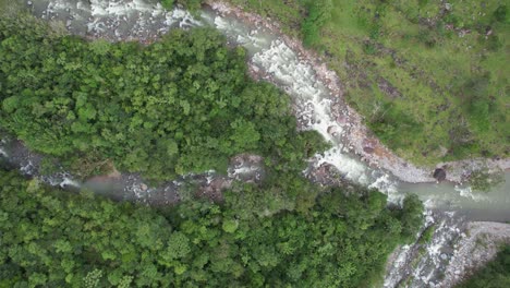 Aerial-orbit-lowering-on-rocky-river-flowing-through-green-meadow-and-woods,-General-Viejo,-Costa-Rica