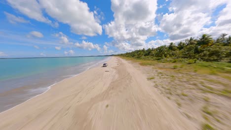 Dynamic-fpv-flight-on-the-beach-of-Miches-town,-following-a-gray-mini-cooper-on-the-shore-of-the-beach