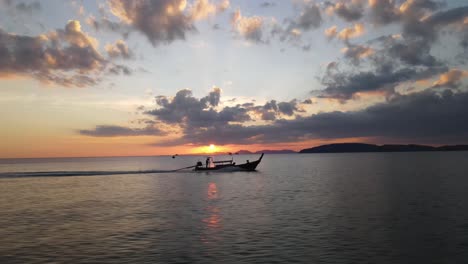 Traditionelles-Boot,-Das-Mit-Hoher-Geschwindigkeit-Durch-Das-Meer-Segelt,-Mit-Einem-Wunderschönen-Sonnenuntergang-Direkt-über-Den-Silhouetten-Der-Hügellandschaft-Von-Krabi