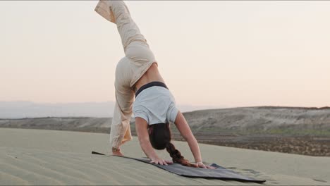 Young-brunette-yoga-instructor-on-a-sand-hill-performing-a-yoga-routine-early-in-the-morning