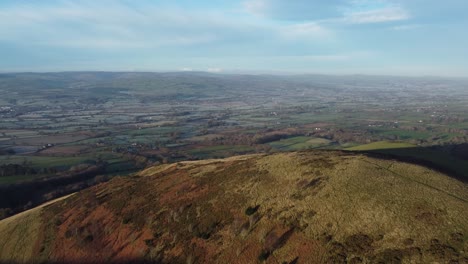 Early-sunlight-on-highland-Welsh-mountain-peak-aerial-view-across-vast-frosty-idyllic-farmland-countryside-rising-forward