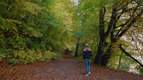 Young-Tall-Guy-With-Cap-Walks-With-Hands-in-Pockets-on-a-Path-into-The-Gyllebo-Forest-in-Autumn,-South-Sweden-Österlen---Static-Wide-Shot