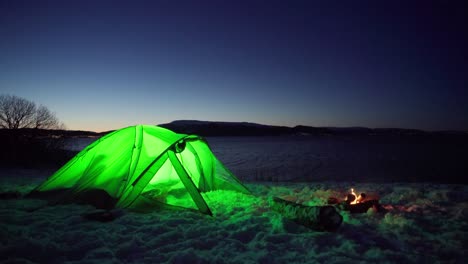 Illuminated-Green-Camping-Tent-With-Camp-Fire-At-Night