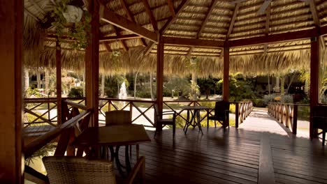 Thatched-wooden-gazebo-with-tables-and-chairs-built-over-pond,-luxury-resort