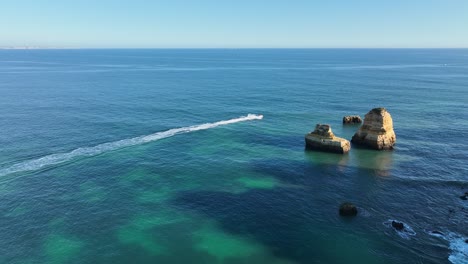 Speedboat-at-Rocky-Coast---Algarve,-Portugal---Stabilized-droneview-in-4K