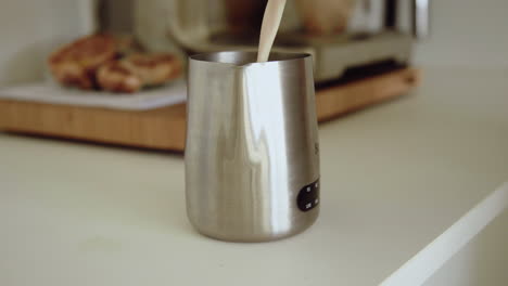 Barista-is-pouring-milk-into-metal-milk-can-preparing-a-cappuccino-at-home-in-the-kitchen