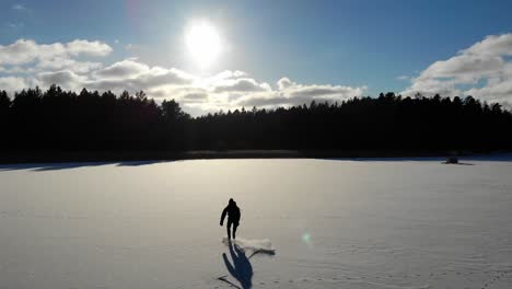 Aerial-view-of-ice-skater-on-a-snow-covered-frozen-lake-in-the-sun