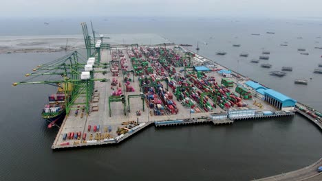 Rotating-aerial-of-industrial-port,-trucks-and-open-ocean-in-Indonesia