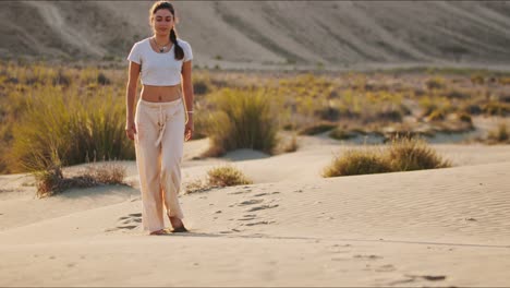 Young-brunette-yoga-instructor-walking-towards-the-camera-on-a-sand-hill-early-in-the-morning