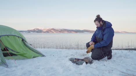 Hombre-Arrodillado-Frente-Al-Fuego-Del-Campamento-En-Un-Día-Frío-En-Invierno