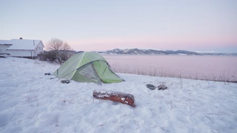 Camper's-Tent-And-A-Piece-Of-Wood-Log-On-Snow-By-The-Lakeshore