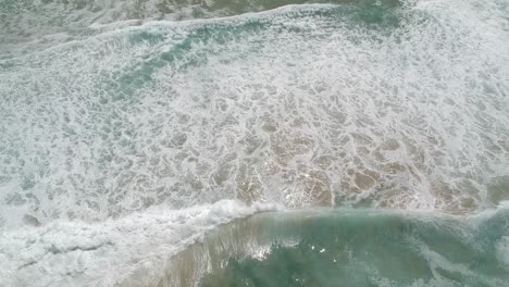 Following-waves-onto-a-beach-with-a-drone,-high-angle-view