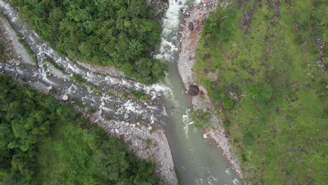 Aerial-rising-on-rocky-river-flowing-between-green-meadow-and-dense-forest,-General-Viejo,-Costa-Rica