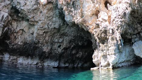 Scuba-diver-swimming-out-of-a-sea-cave-looking-up-at-the-impressive-rocky-cliff-around-him,-Vis-island,-Adriatic-Sea,-Croatia