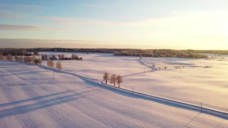 Country-side-road-during-cold-snowy-winter-season,-golden-sunset,-aerial-drone-shot