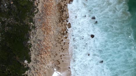 Foamy-waves-crashing-into-a-rocky-shoreline,-view-from-drone-above