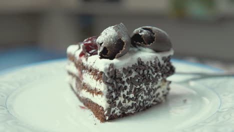 Appetizing-chocolate-and-cream-cake-slice-rotates-on-plate-with-cherries