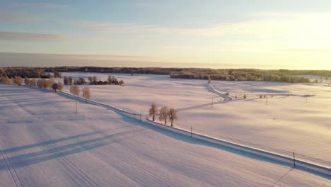 Iconic-rural-road-under-snow-layer-during-golden-sunset,-aerial-drone-shot