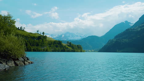 Picturesque-view-of-lake-in-Brienz-Switzerland-at-noon-as-water-ripples-calming-move-towards-shore-with-cloudy-mountains-in-the-distance-in-Europe,-wide-view