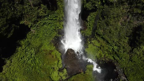 Aerial-dolly-out-of-Salto-El-Leon-waterfall-falling-into-rocky-natural-pool-surrounded-by-green-dense-woods,-Pucon,-Chile