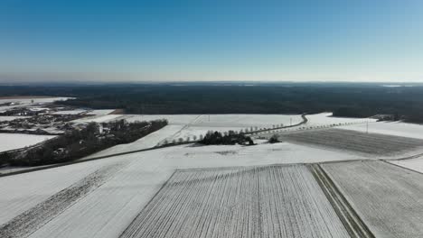 Flight-over-a-snowy-field-under-blue-sky-in-4K-with-a-forest-at-horizon
