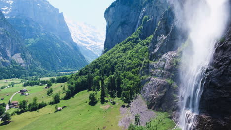 Calming-drone-shot-hovering-near-large-iconic-waterfall-flowing-into-valley-at-noon-in-Lauterbrunnen,-Switzerland,-Europe,-wide-view