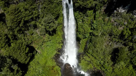 Aerial-pan-right-of-Salto-El-Leon-waterfall-streaming-on-rocky-pool-surrounded-by-dense-green-forest,-Pucon,-Chile