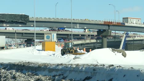 Cargador-Limpiando-La-Nieve-En-La-Carretera-Con-Tráfico-En-La-Distancia-En-Invierno-En-Montreal,-Canadá