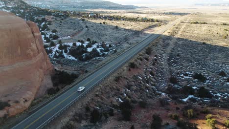 DRONE-FOLLOWING-WHITE-CAR-IN-MOAB-UTAH-WITH-MOUNTAINS-AND-SNOW-ON-ROADTRIP