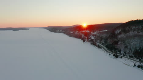 Winterluftbild-über-Einem-Zugefrorenen-Fluss,-Während-Die-Sonne-Hinter-Den-Hügeln-Untergeht