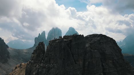 Fünf-Bergsteiger-Auf-Dem-Di-Lavaredo-Am-Kreuz,-Während-Im-Hintergrund-Das-Teilweise-Bewölkte-Tre-Cime-Auftaucht