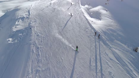 Aerial-drone-view-of-skiers,-downhill-skiing-down-snowy-slopes-in-the-sunny-alps---tilt,-drone-shot