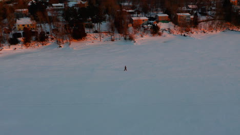 Luftaufnahme-Einer-Person,-Die-Bei-Sonnenuntergang-Entlang-Eines-Zugefrorenen-Flusses-Schneeschuhwandern-Geht